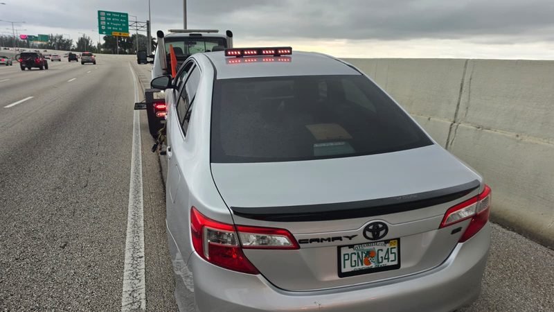 Toyota Camry plateado detenido en la banquina de una autopista de Miami con la barra de luces de la grúa encendida