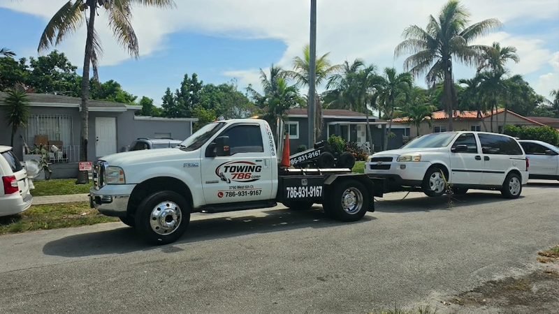Grúa blanca de Towing 786 remolcando una minivan en una calle residencial de Hialeah con palmeras